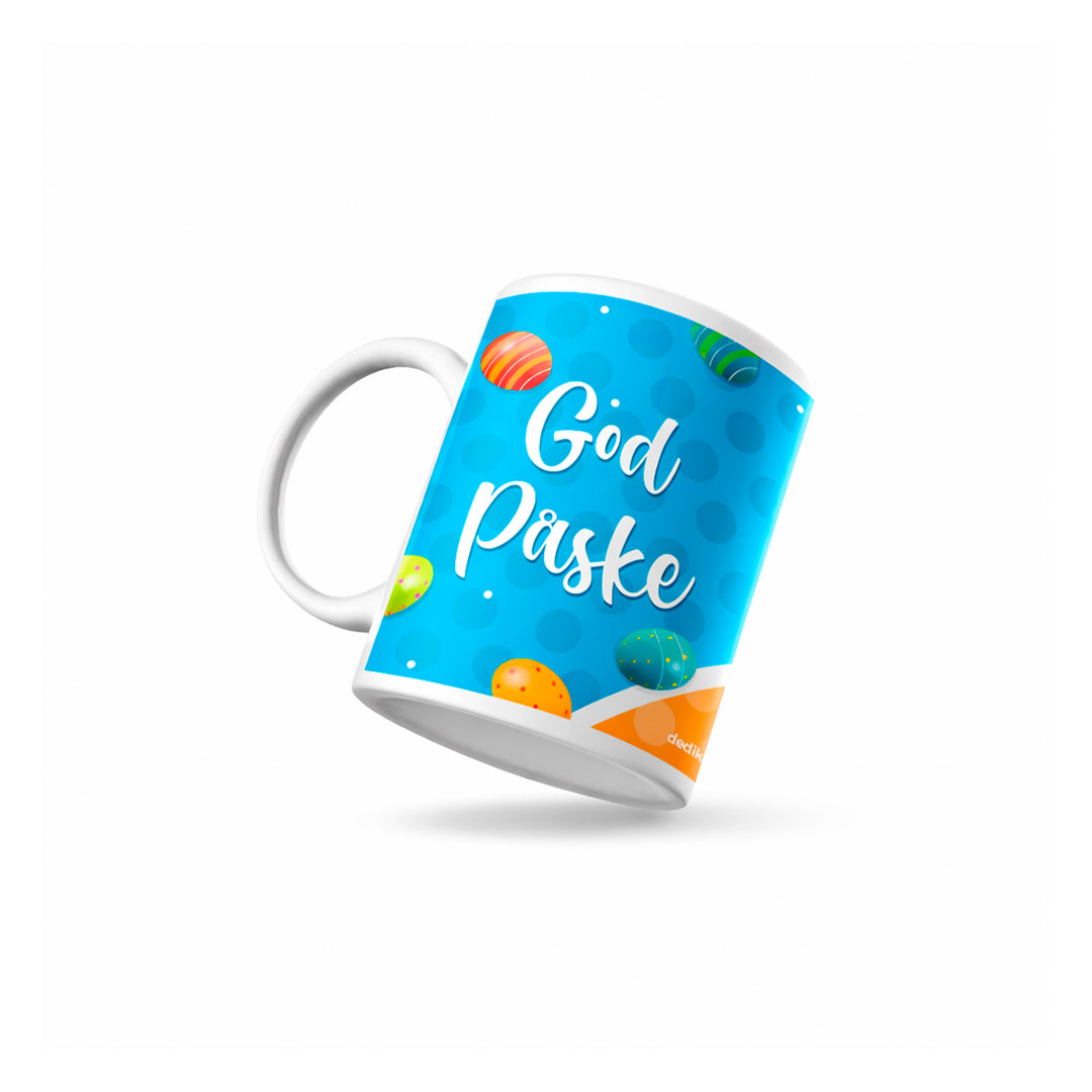 Håndlaget påskekopp med God Påske-design, vist i skrå vinkel med blå bakgrunn og fargerike påskeegg